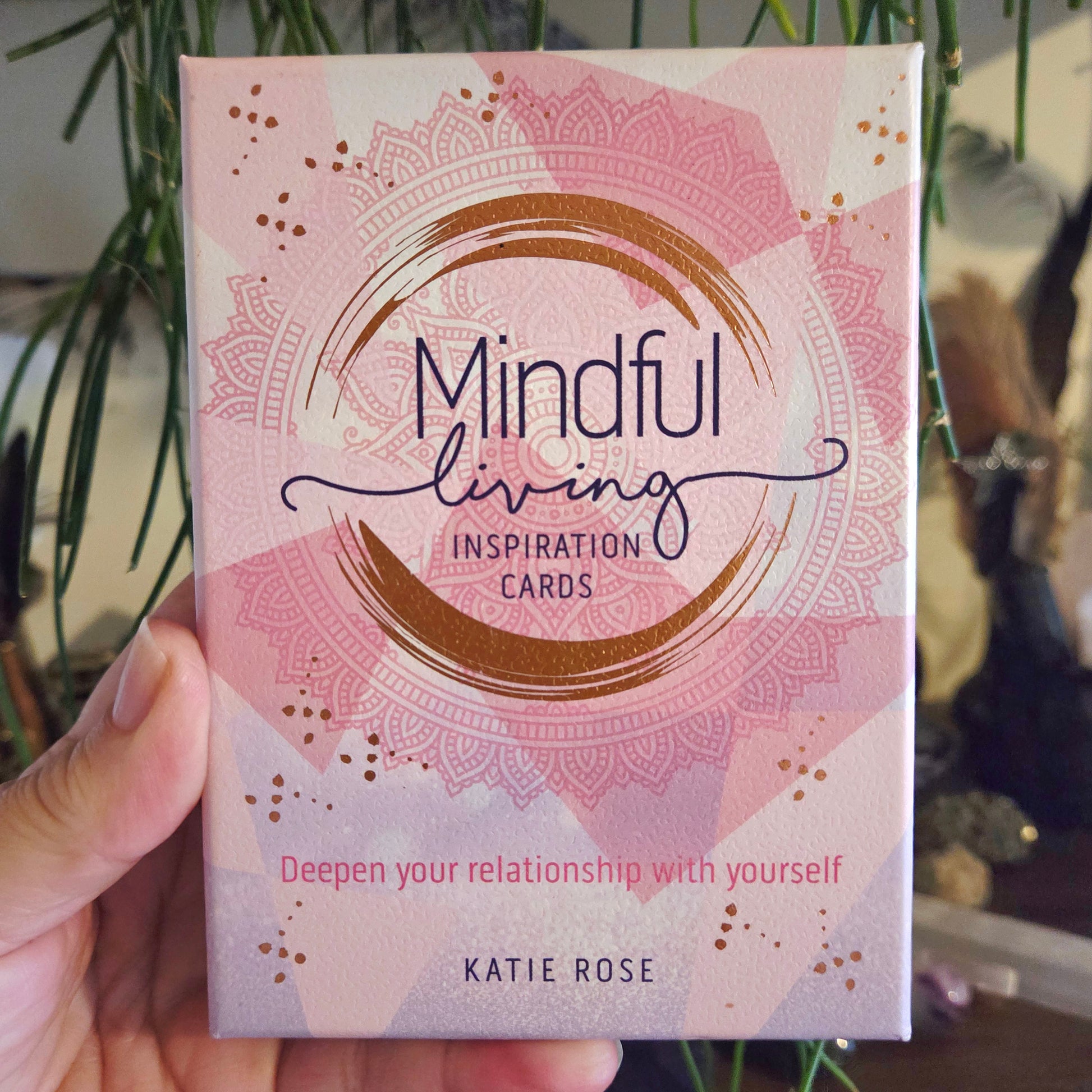 A person holding a pack of 'Mindful Living Inspiration Cards' with decorative patterns and text on the cover.