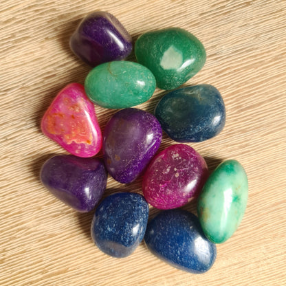 A collection of various colored agate tumble stones displayed on a wooden surface.