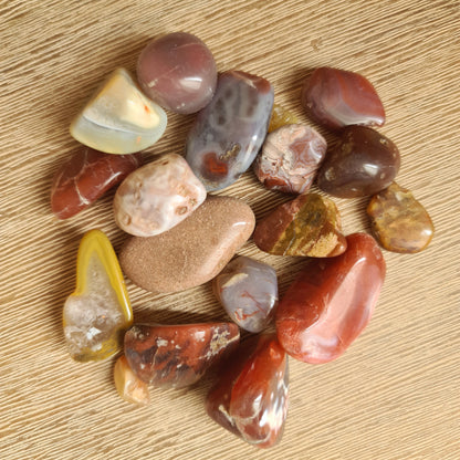 A collection of various colored agate tumble stones arranged on a wooden surface.