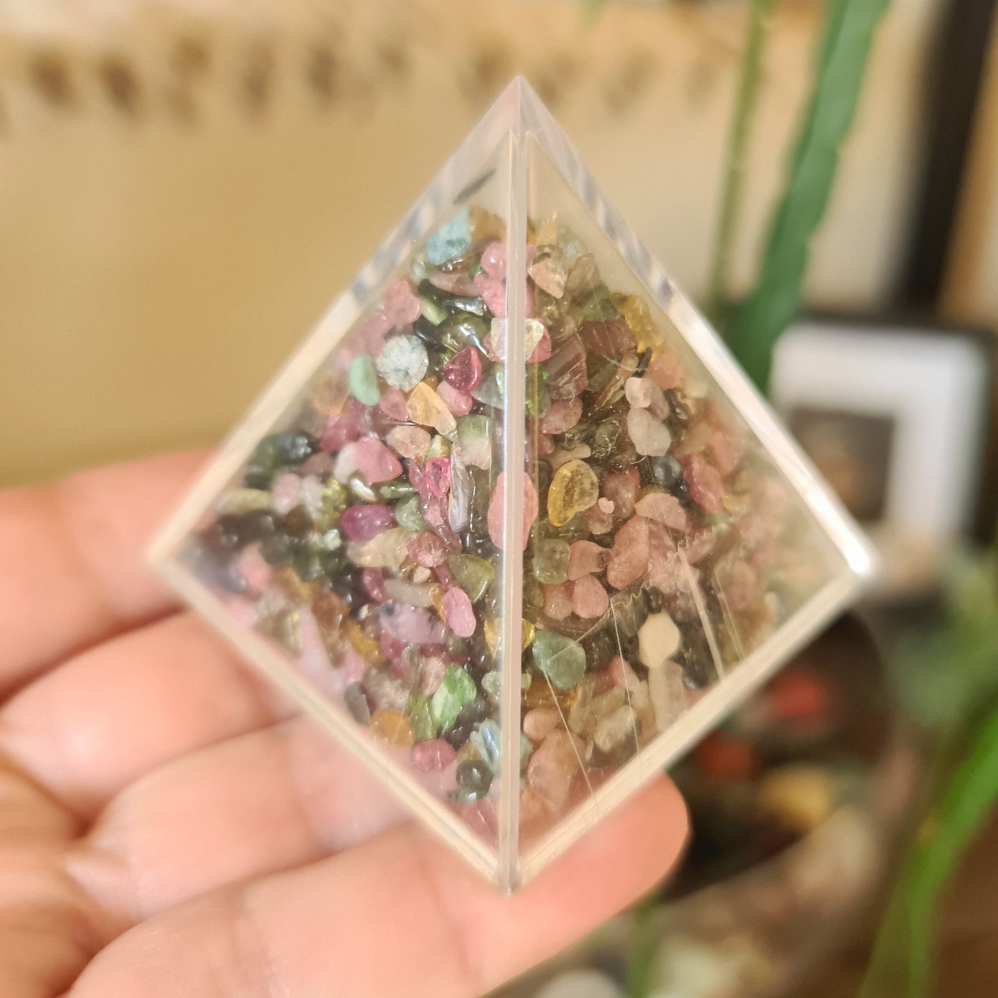 A triangular-shaped clear crystal with mixed tourmaline stones visible inside, held in a hand.