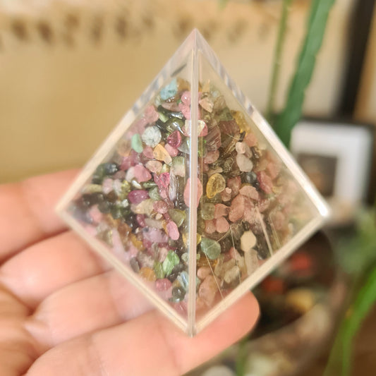 A triangular-shaped clear crystal with mixed tourmaline stones visible inside, held in a hand.