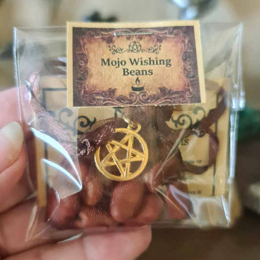 A pouch containing seven large, brown mojo wishing beans with a gold pentagram charm, packaged in a clear plastic bag with a label reading 'Mojo Wishing Beans'.