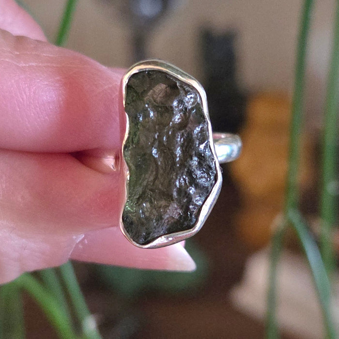 Silver ring with a natural stone design held by a hand against a blurred background