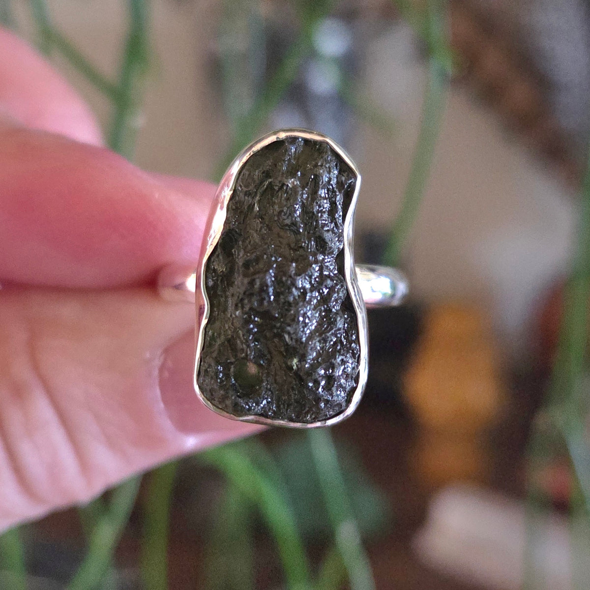 Silver ring with a large, rough-textured stone held by a hand against a blurred natural background.