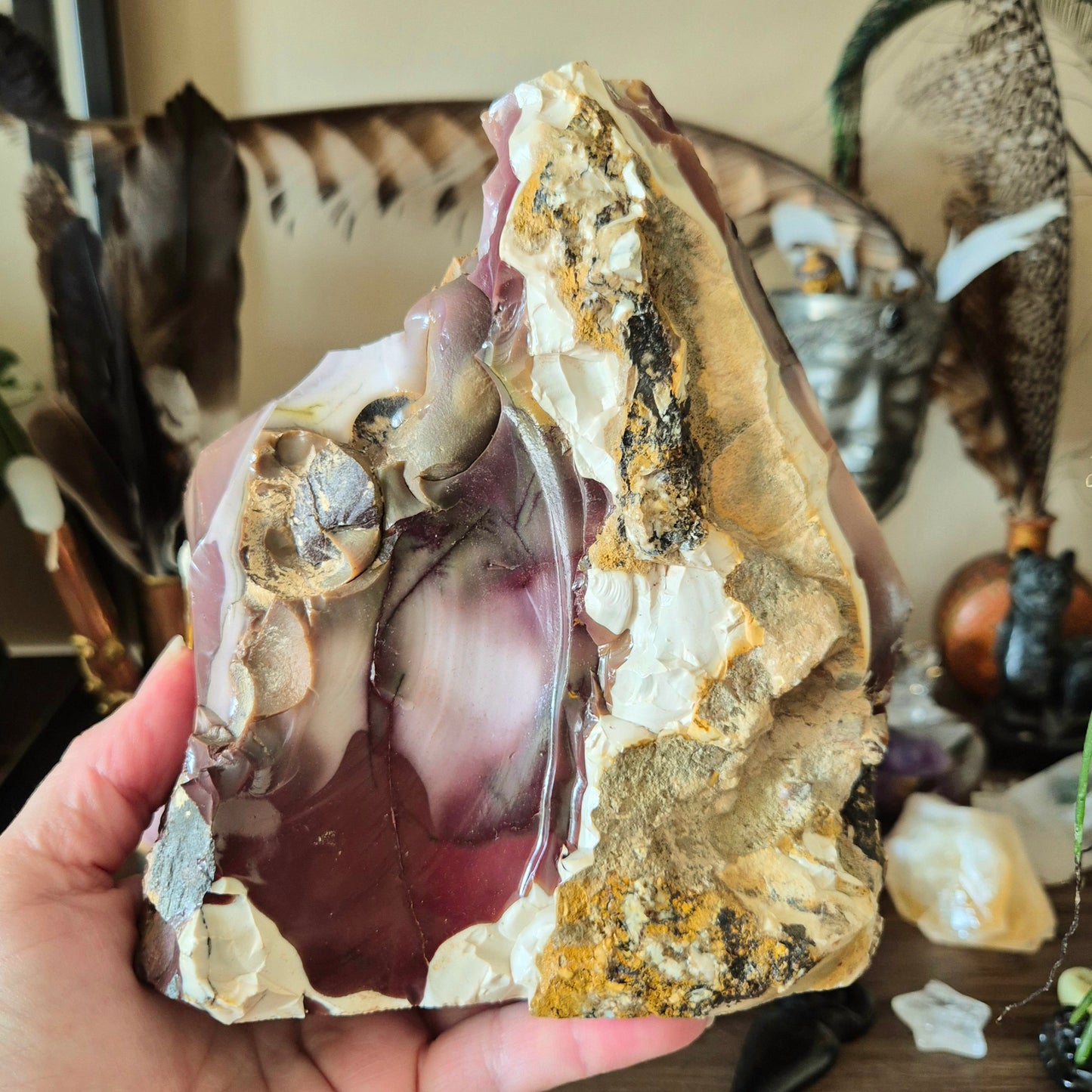 A freeform Mookaite Jasper stone held in a person's hand, with a variety of natural colors including purple, pink, brown, and white.