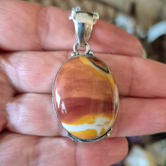 This image features a Mookaite Jasper Pendant, elegantly displayed against a softly lit background. The pendant showcases a captivating blend of earthy red, orange, and yellow hues, with a striking contrast against the cooler tones of black and gray.