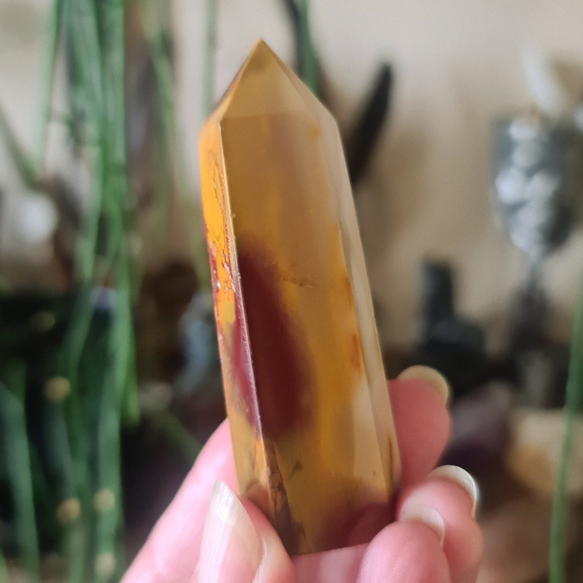 A polished Mookaite Jasper point held in a person's hand, with a yellow to orange gradient color.