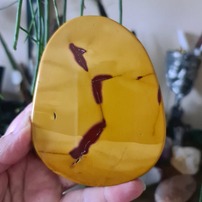 A slab of Mookaite Jasper with yellow and red hues, held in a person's hand.