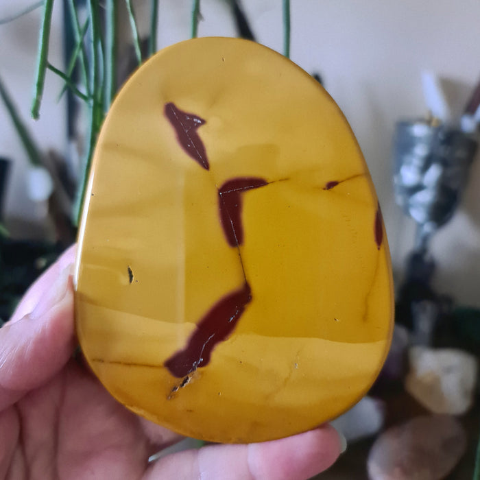A slab of Mookaite Jasper with yellow and red hues, held in a person's hand.