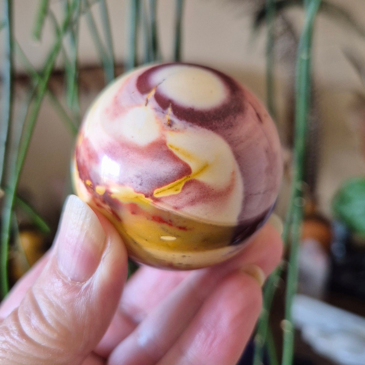 A person holding a Mookaite Jasper Sphere with a marbled multicolor pattern.