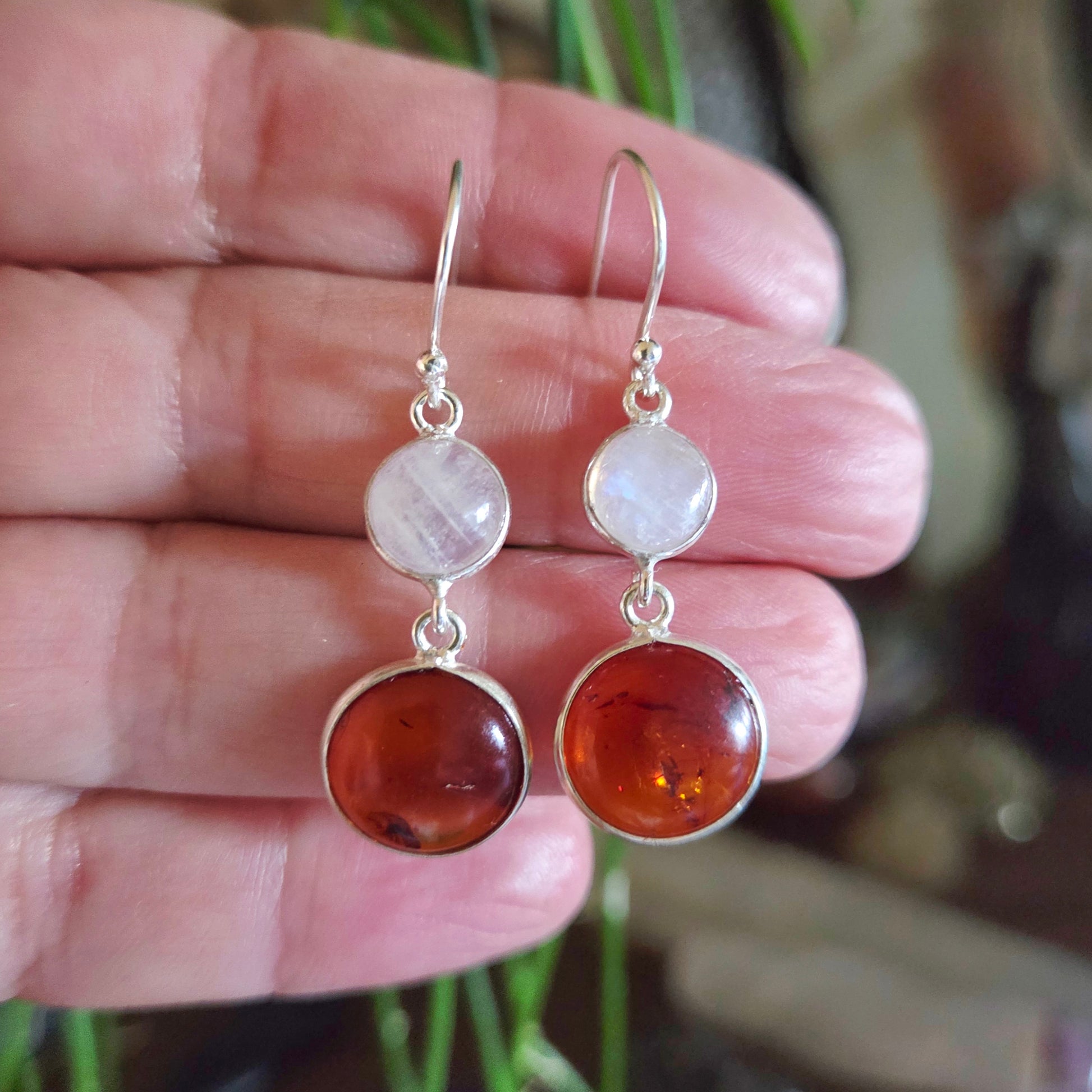 amber and moonstone earrings held between fingers with a blurred background