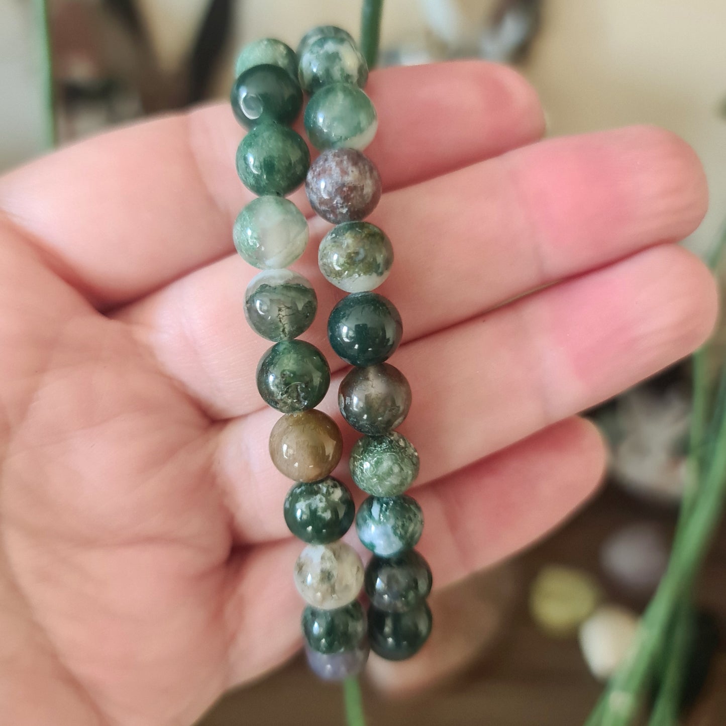 A hand holding a moss agate bracelet with a mix of green and brown colors and patterns.