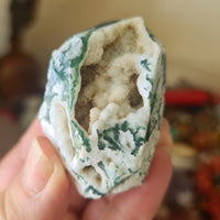 A polished green moss agate druzy freeform gemstone, held in a person's hand.