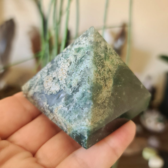 A polished green moss agate crystal with a pyramidal shape, held in a person's hand.