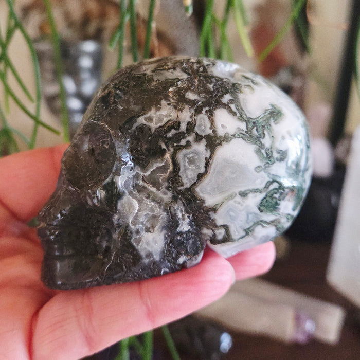 A hand holding a small, polished skull-shaped rock with a pattern of gray and black marbling.