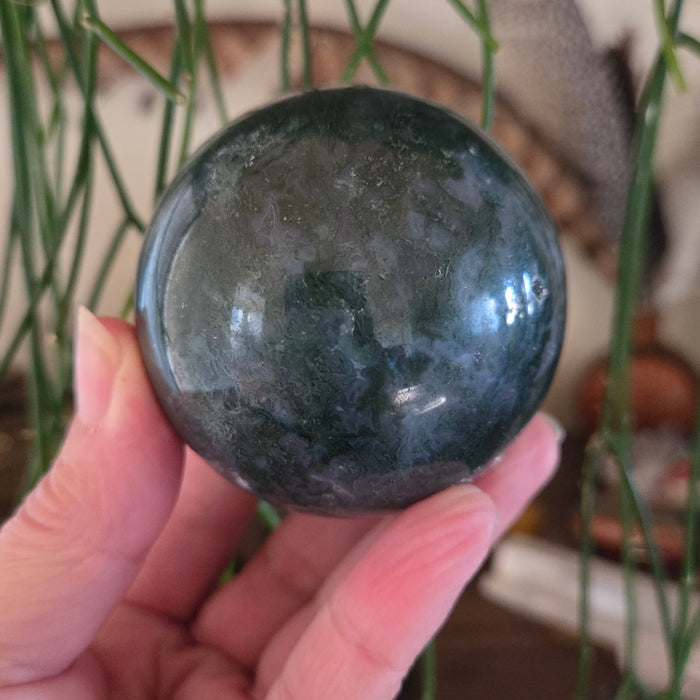 Hand holding a dark green stone sphere with a blurred indoor background