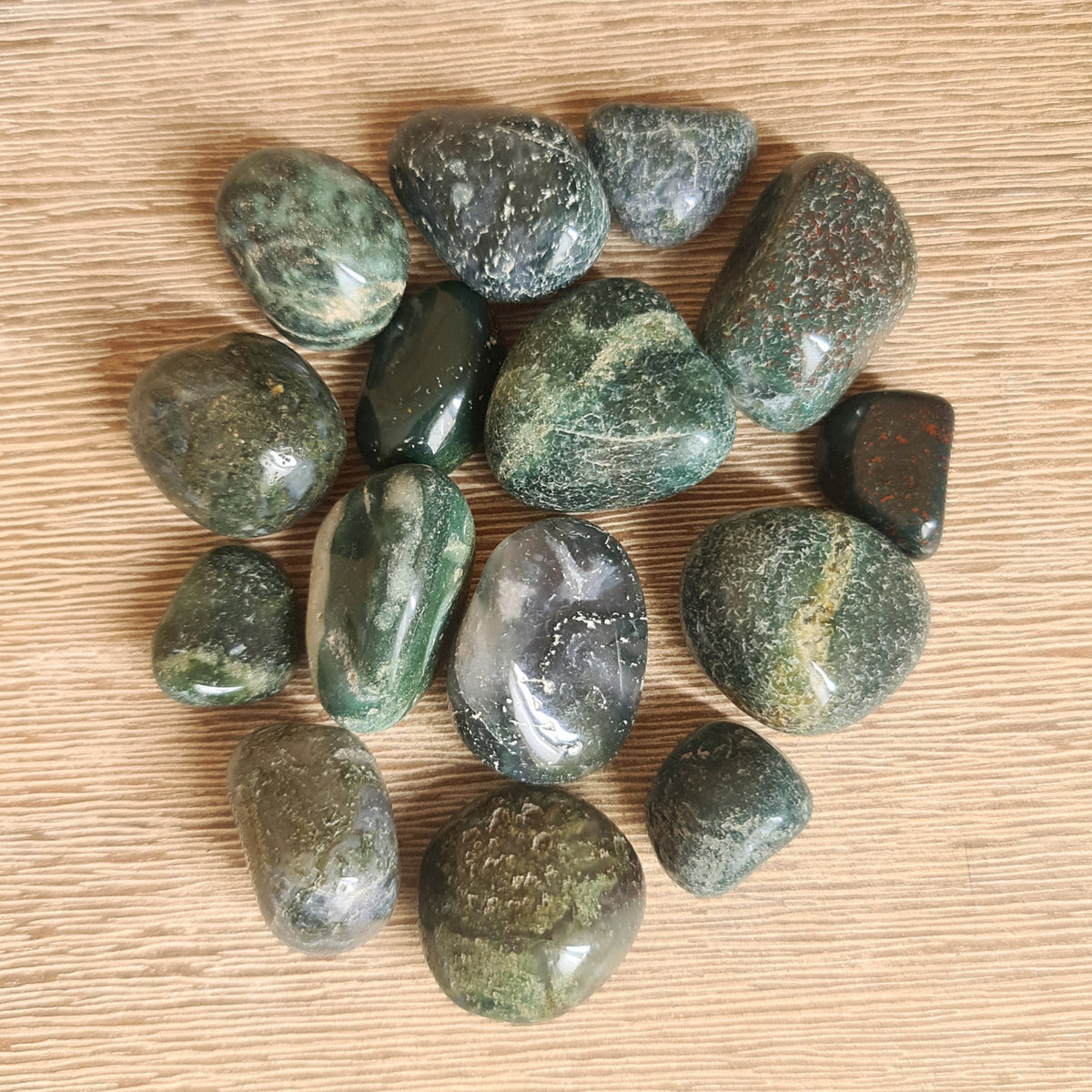 A collection of polished moss agate tumbles with varying shades of green and brown, displayed on a wooden surface.