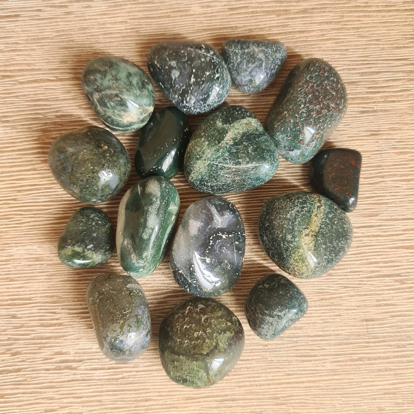 A collection of polished moss agate tumbles with varying shades of green and brown, displayed on a wooden surface.