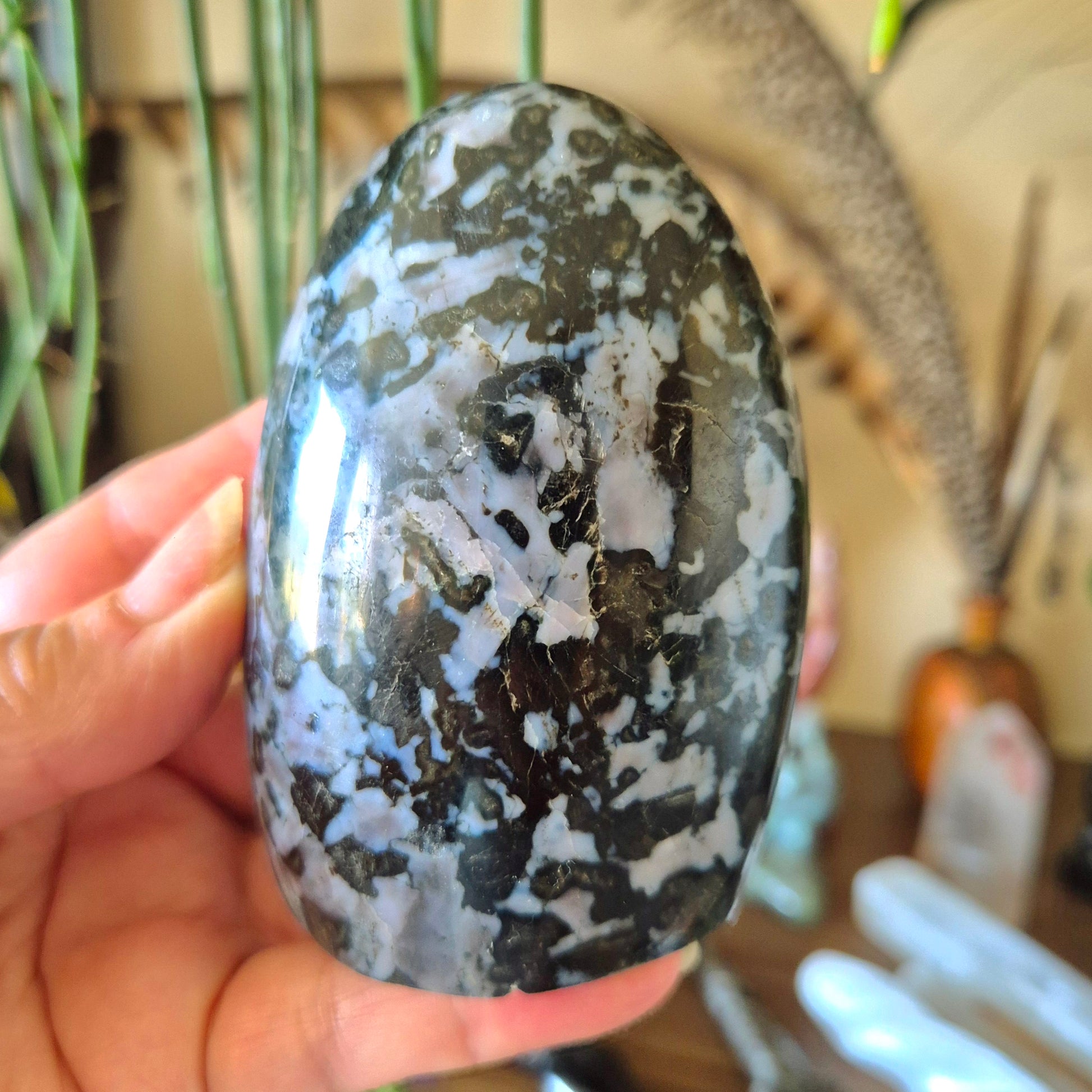 A polished freeform merlinite stone with a camouflage-like pattern, held in a person's hand.