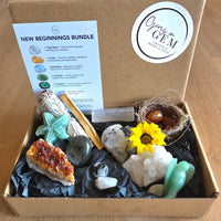 A Geng GEM 'New Beginnings Bundle' gift box filled with various crystals, stones, a small bird nest with two brown eggs, a yellow sunflower, and a printed guide card explaining the bundle contents.