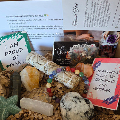 A crystal and affirmation gift bundle arranged on a wood tray, featuring a white sage bundle wrapped in string, a multicolor beaded bracelet, polished crystals, a black sachet, cards with affirmations, and a purple amethyst cluster.