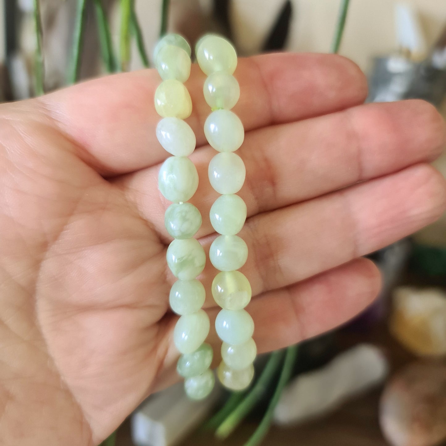 A hand holding a bracelet with polished green jade beads.
