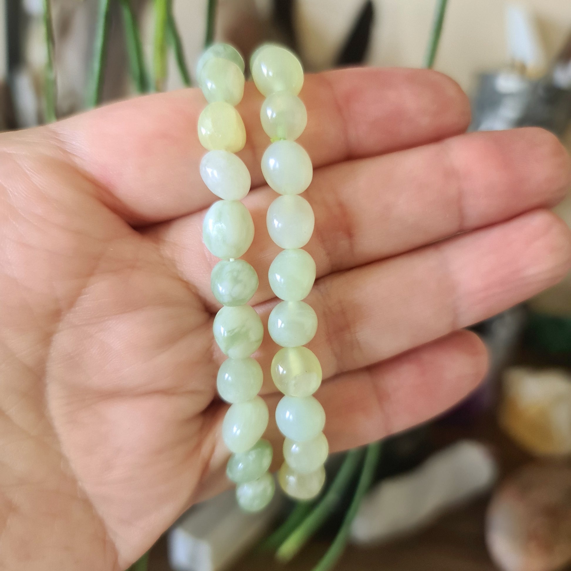 A hand holding a bracelet with polished green jade beads.