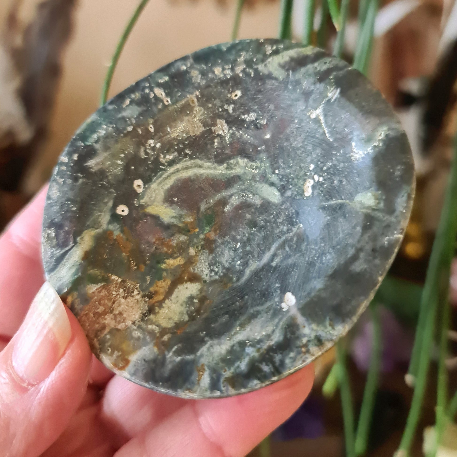 A polished Ocean Jasper stone with a green and brown color pattern, held in a person's hand.