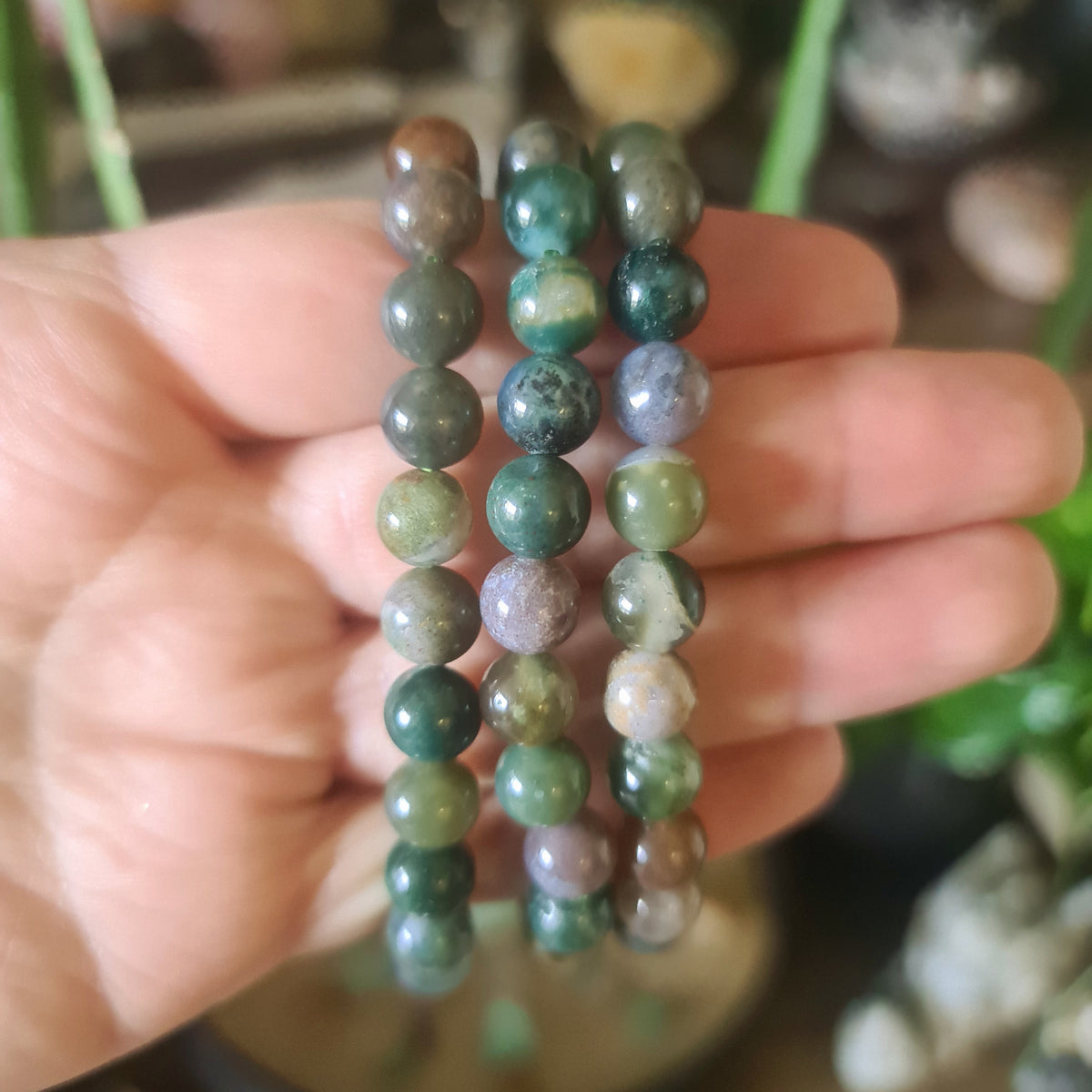 A multicolored beaded bracelet held in a person's hand, featuring various shades of green, brown, and pink.