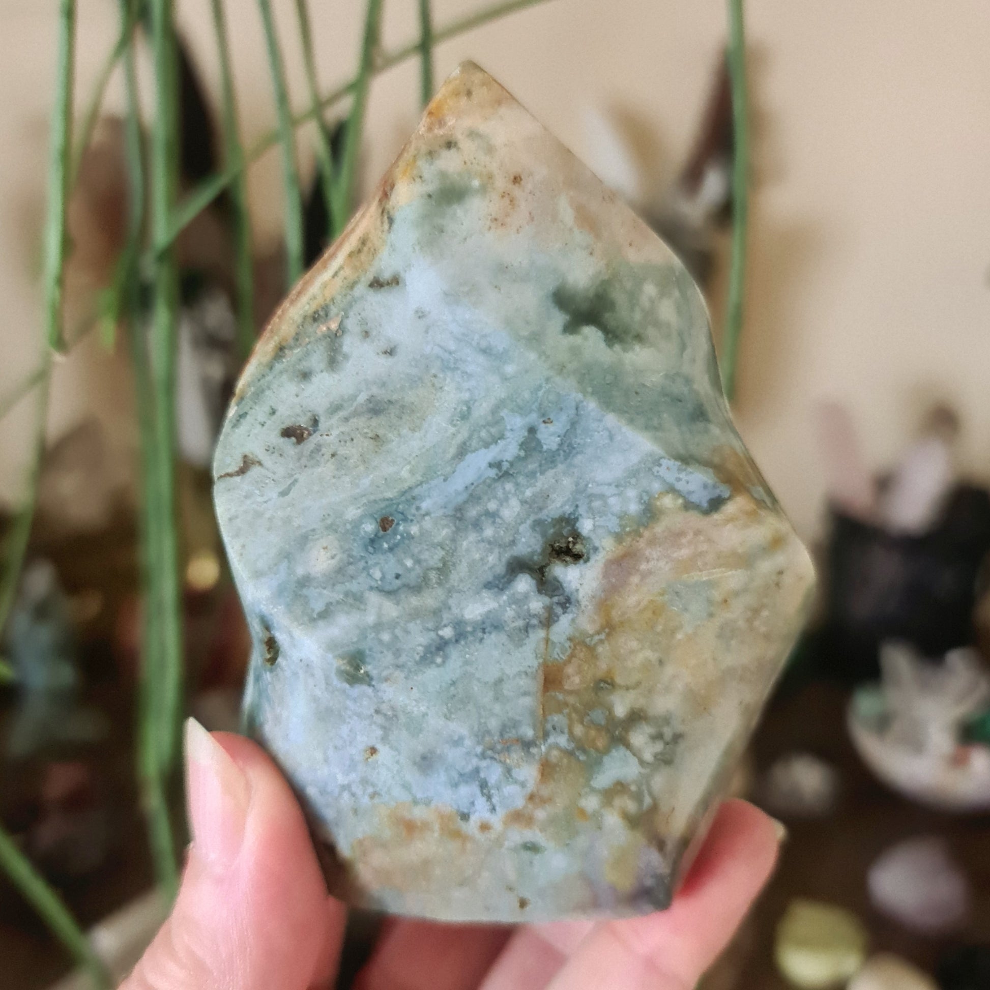 A polished Ocean Jasper crystal with a blue and green color pattern, held in a person's hand.