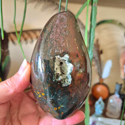 A polished freeform Ocean Jasper stone weighing 580 grams, held in a person's hand.
