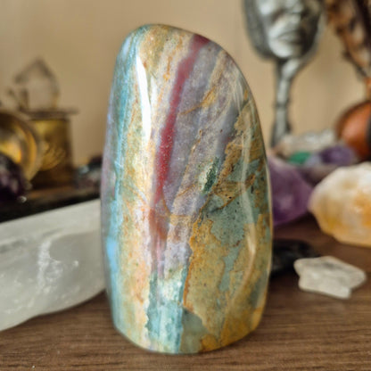 A freeform Ocean Jasper stone with a striped pattern of green, red, and white, placed on a wooden surface.