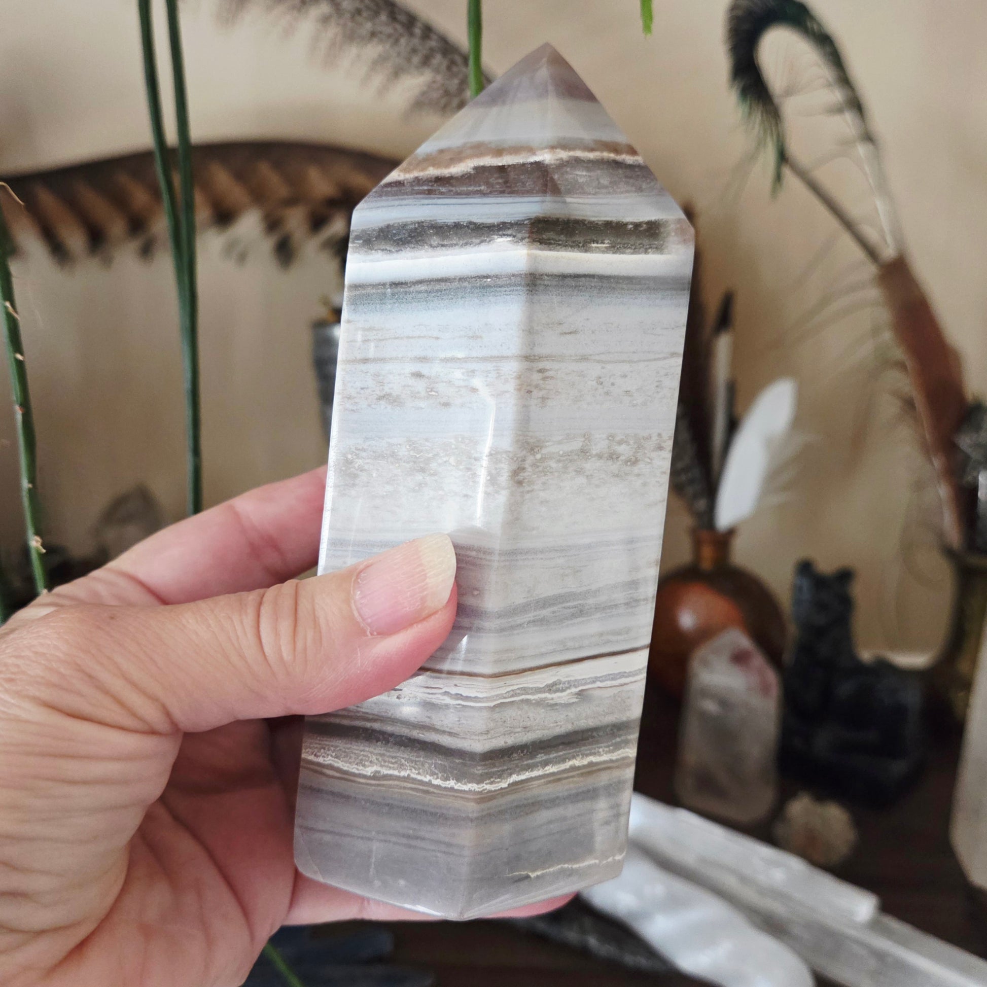 A hand holding a polished Ocean Jasper obelisk tower crystal.