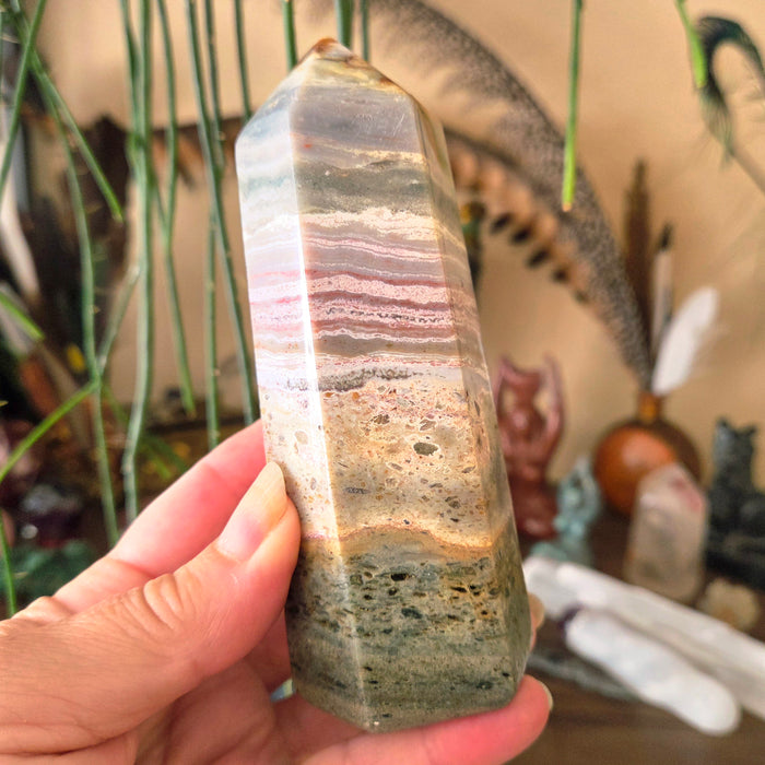A hand holding a polished Ocean Jasper Obelisk Tower with visible layered patterns.