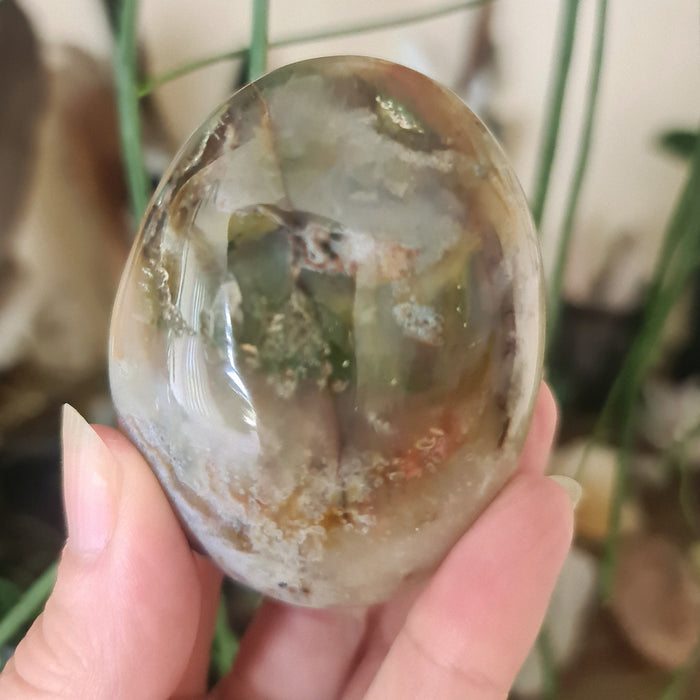 A hand holding a polished Ocean Jasper Palm Stone with a green and brown color pattern.