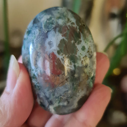 A hand holding a polished Ocean Jasper Palm Stone with a green and brown color pattern.