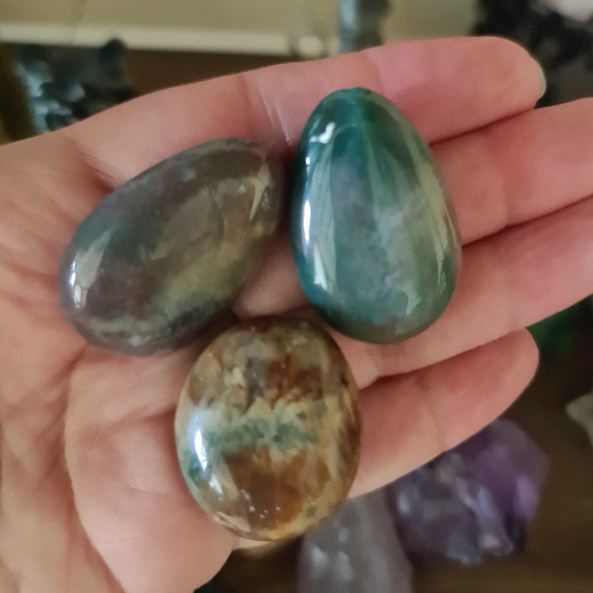 Three polished Ocean Jasper stones held in a person's hand, with varying shades of green and brown.