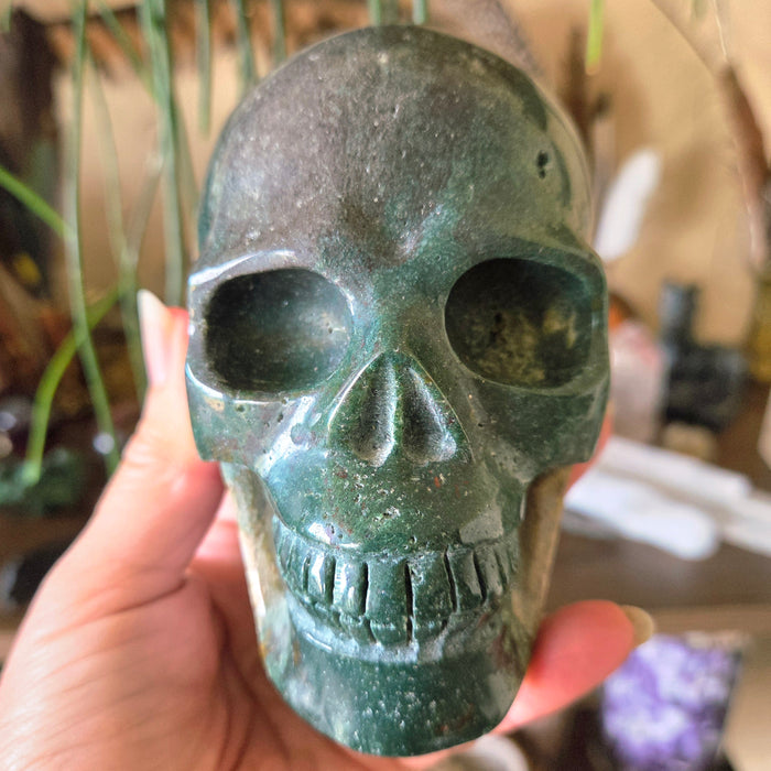 A hand holding a polished green Ocean Jasper skull-shaped stone