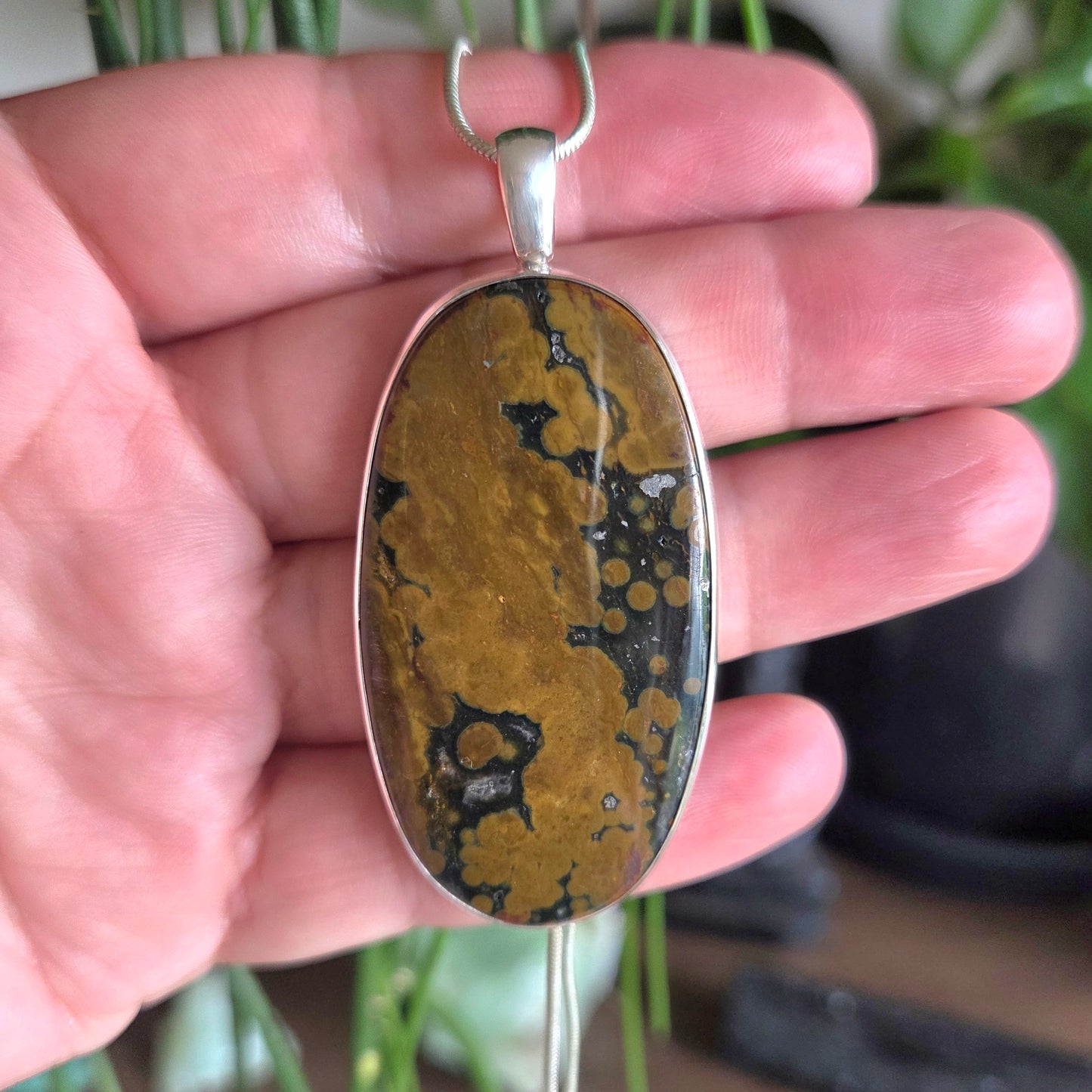 Hand holding a pendant with a marbled stone design and silver frame.