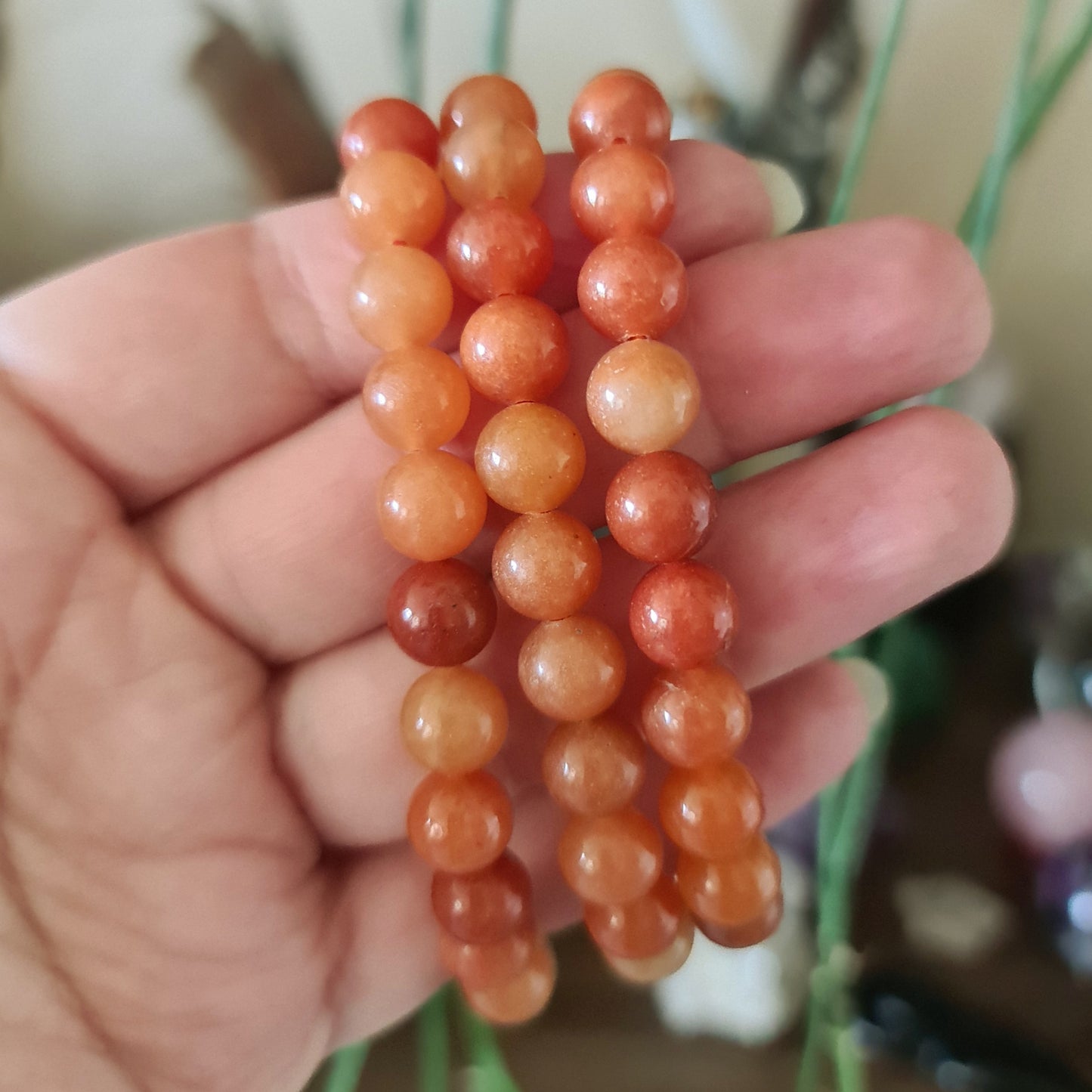 A hand holding a series of orange aventurine beads with a plant in the background.