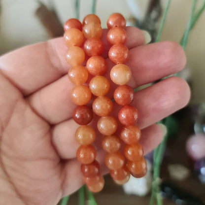 A hand holding a series of orange aventurine beads with a plant in the background.
