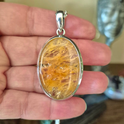 An orange aventurine pendant held in a hand, with a metallic chain attached.