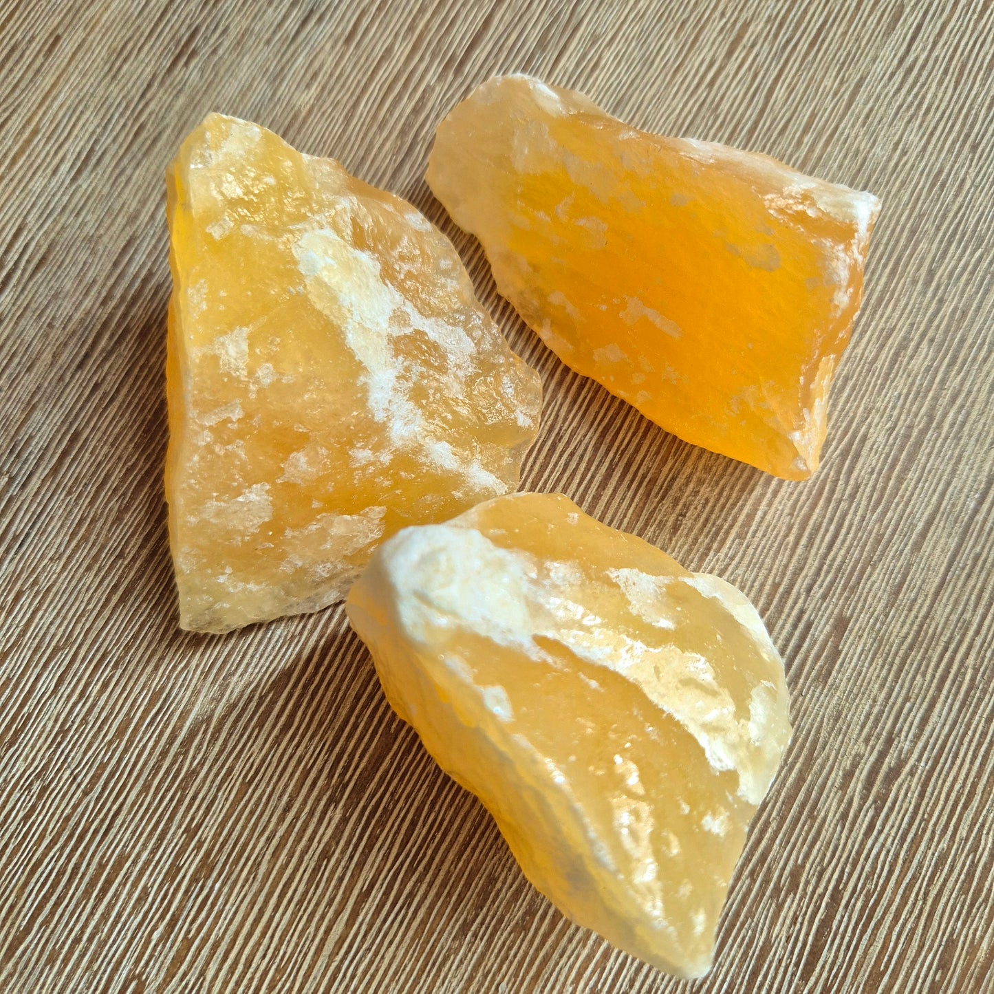 Several polished orange calcite crystals placed on a wooden surface.