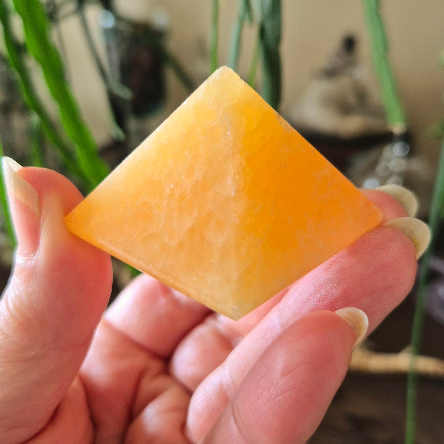 A person holding a small orange calcite pyramid in their hand.