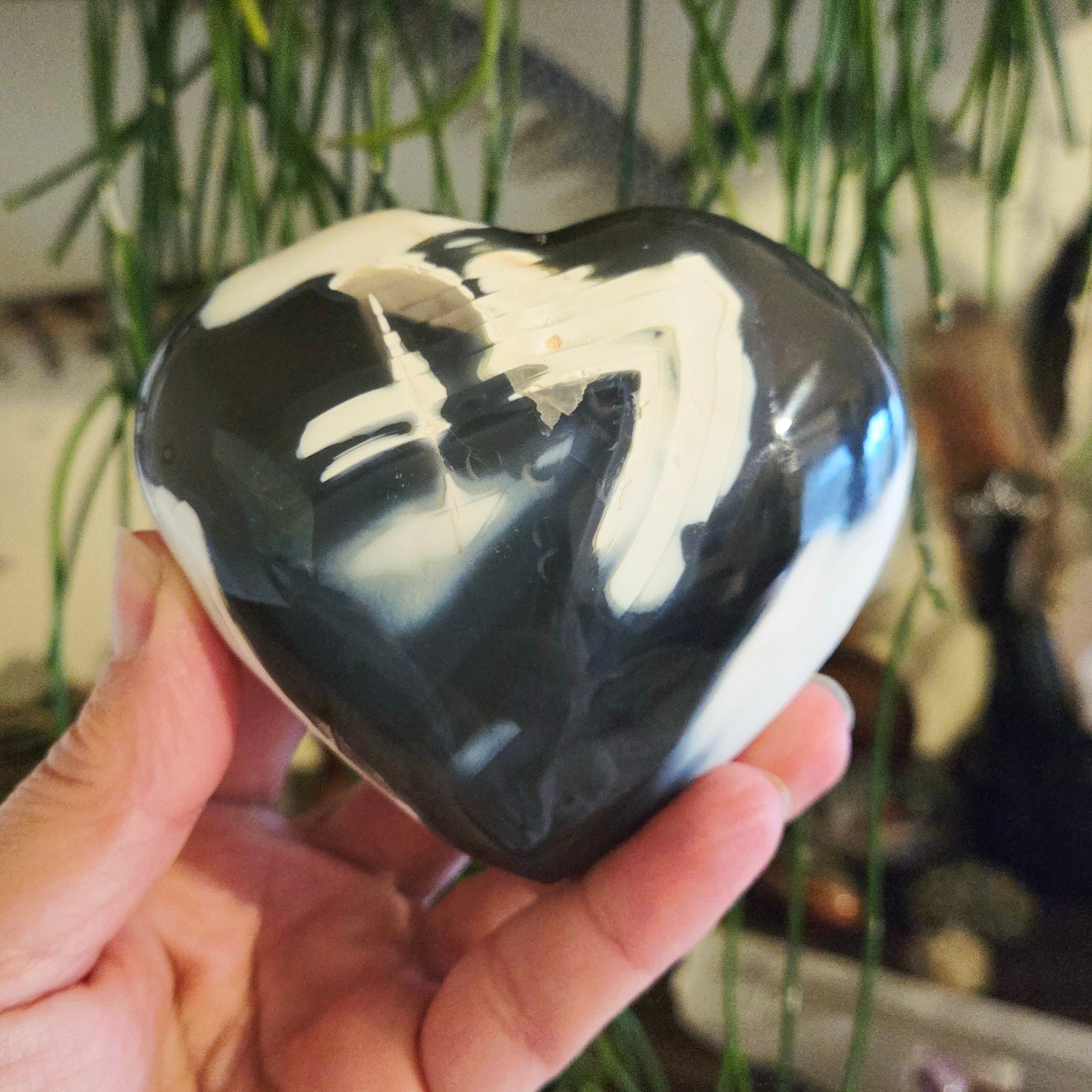 A hand holding a heart-shaped agate stone with black and white patterns.