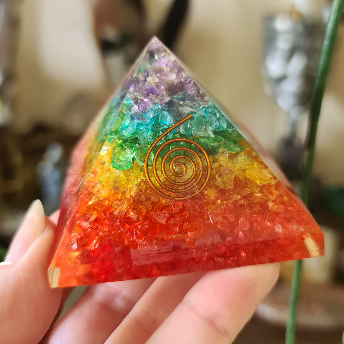 A multicolored Orgonite pyramid with a spiral design on top, held in a person's hand.