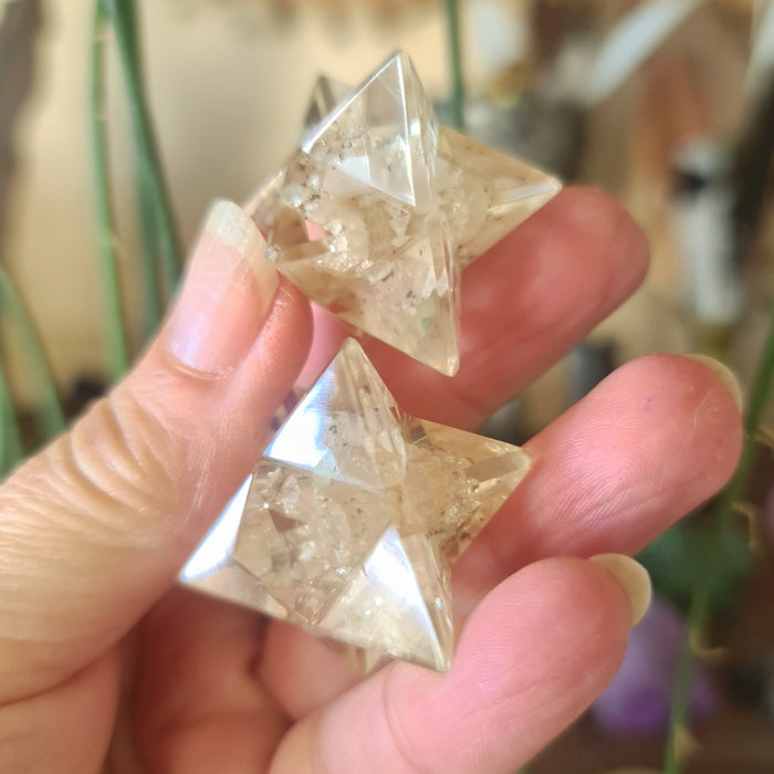 A hand holding a small, clear, star-shaped Orgonite Merkaba with a geometric pattern.