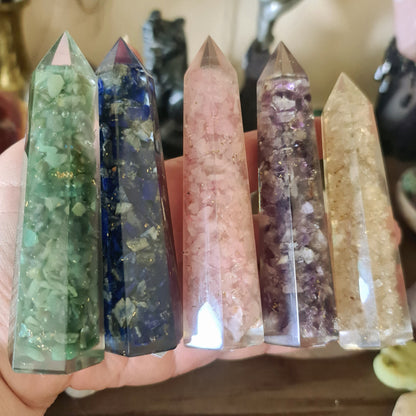 A collection of Orgonite Towers in various colors, each containing embedded crystals, held in a person's hand.