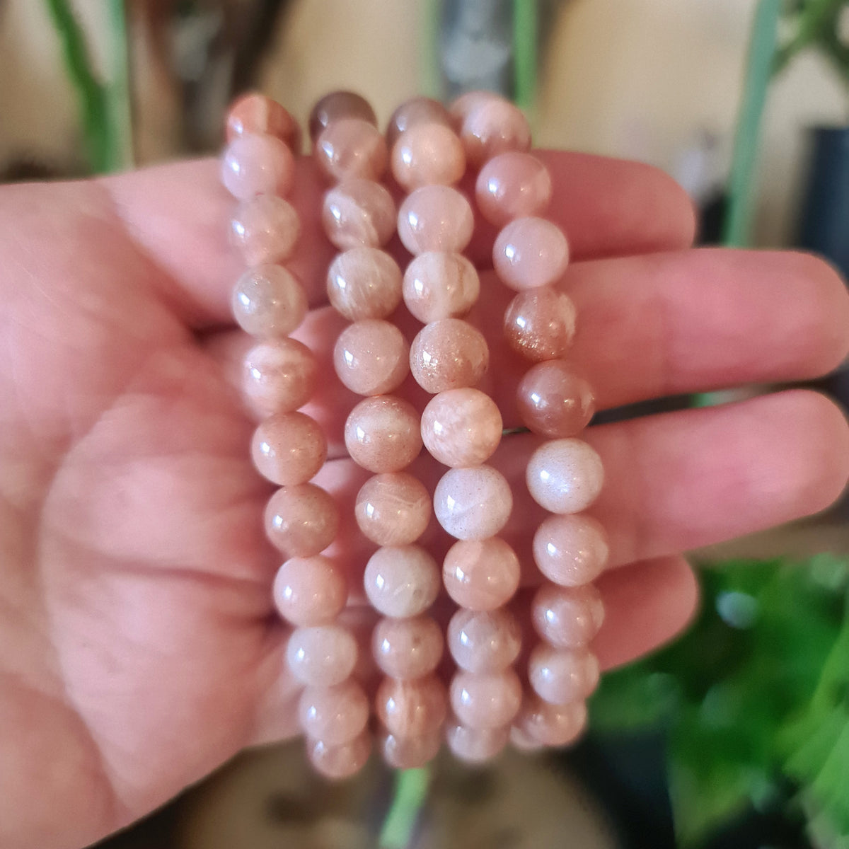 A hand holding a Peach Moonstone Bracelet with round beads.