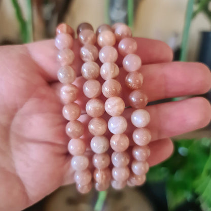 A hand holding a Peach Moonstone Bracelet with round beads.